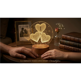 Glowing lamp with heart design on a table with hands reaching towards it, surrounded by books and a photo frame.